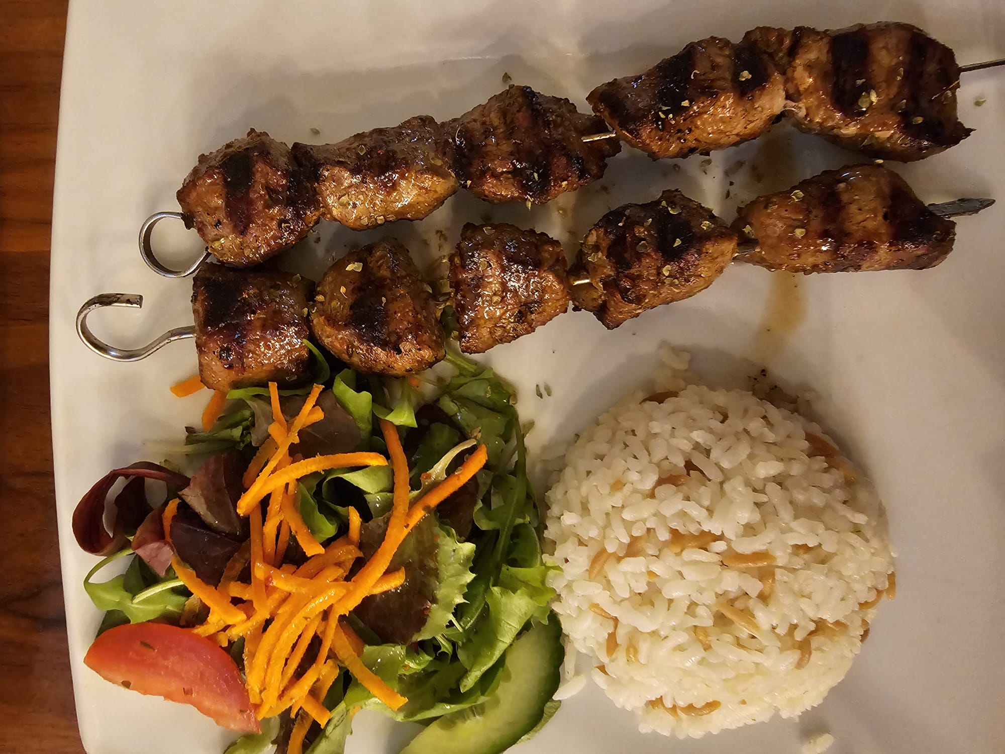 Two skewers of grilled lamb kebabs served with a side of white rice and a fresh garden salad.