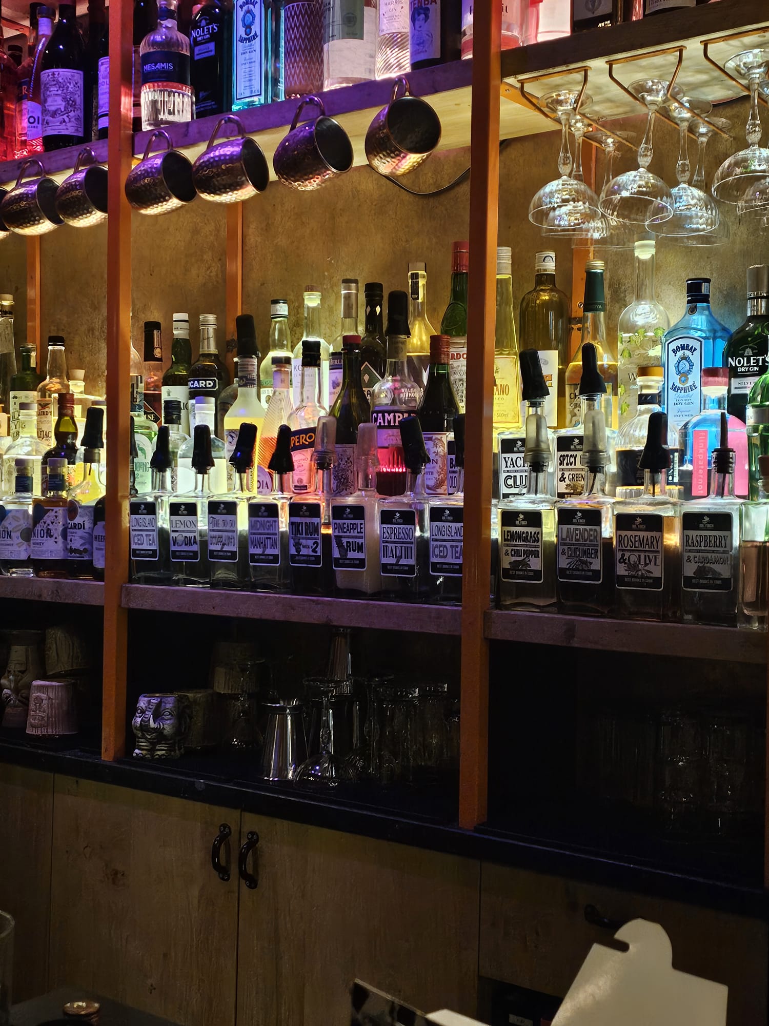 A bar shelf lined with numerous glass bottles of house-infused liquors, each labeled with specific flavors like rosemary or raspberry.