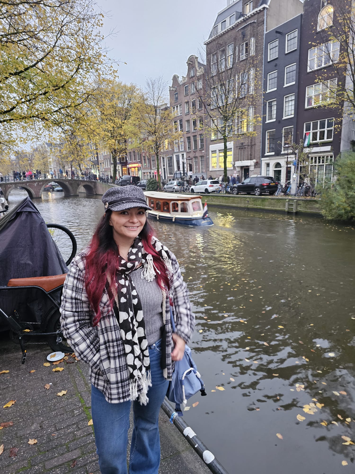 Woman posing in front of a classic Amsterdam canal with a boat and historic Dutch townhouses in the background