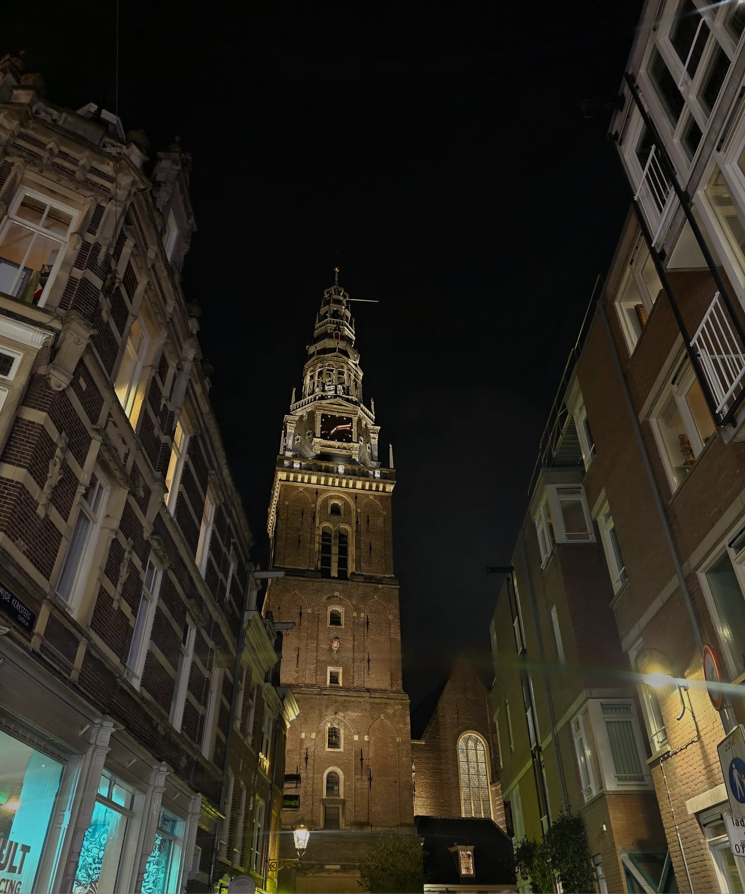 Looking up at the Oude Kerk tower lit up against a dark night sky in Amsterdam's city center