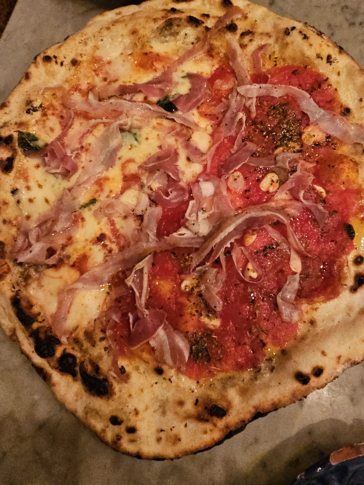 A thin-crust gluten-free pizza topped with tomato sauce, melted mozzarella, and thin ribbons of prosciutto.