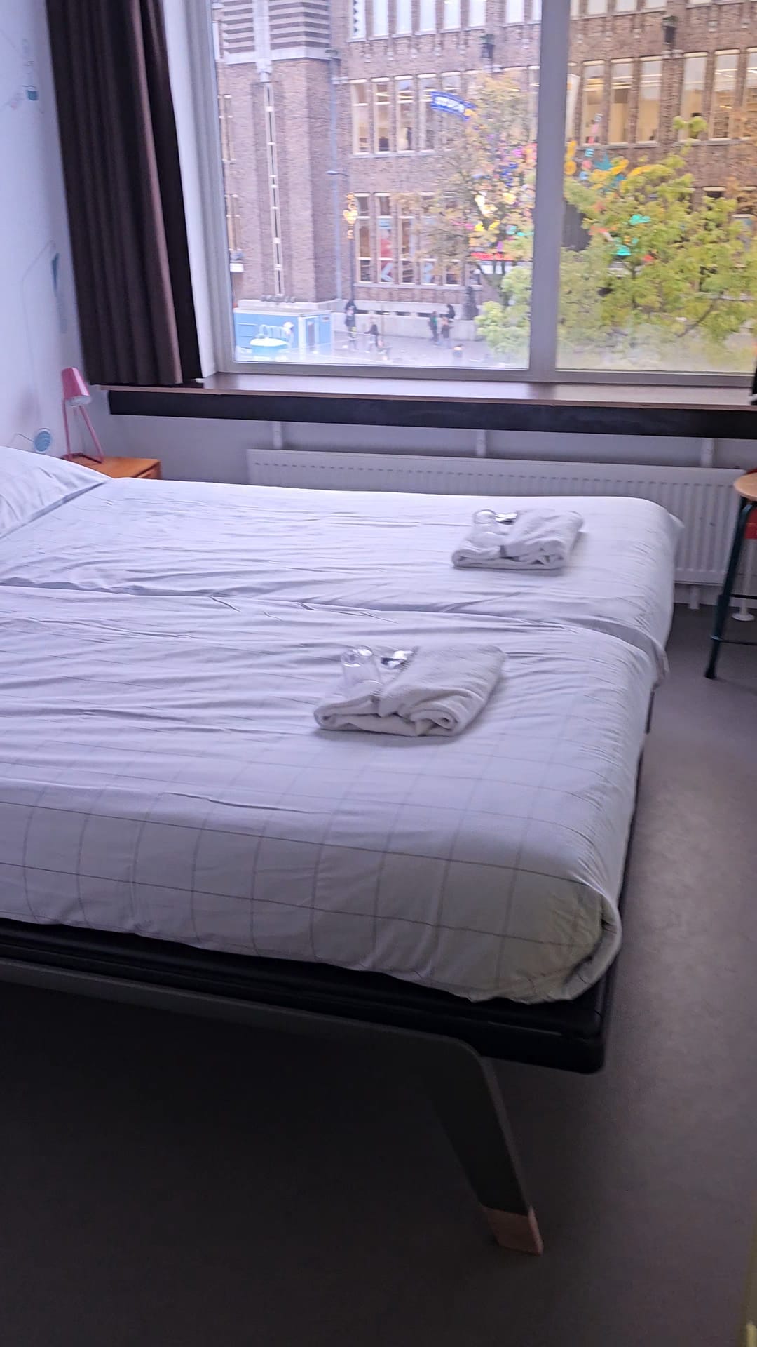 Simple private hostel room with a double bed, folded towels, and a large window overlooking Utrecht city center at StayOk hostel