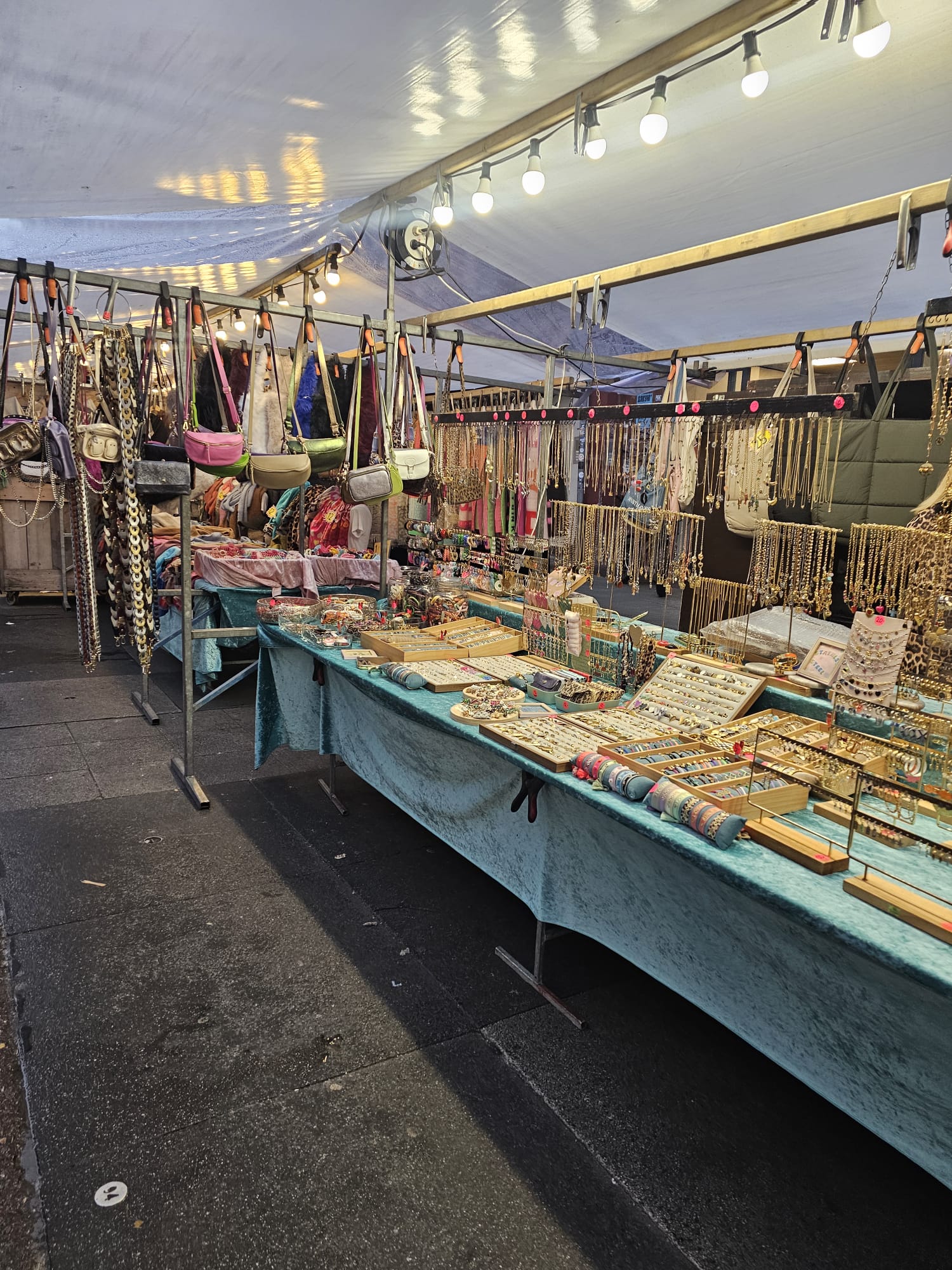Rows of colorful jewelry and accessories spread across tables at an outdoor street market in Amsterdam