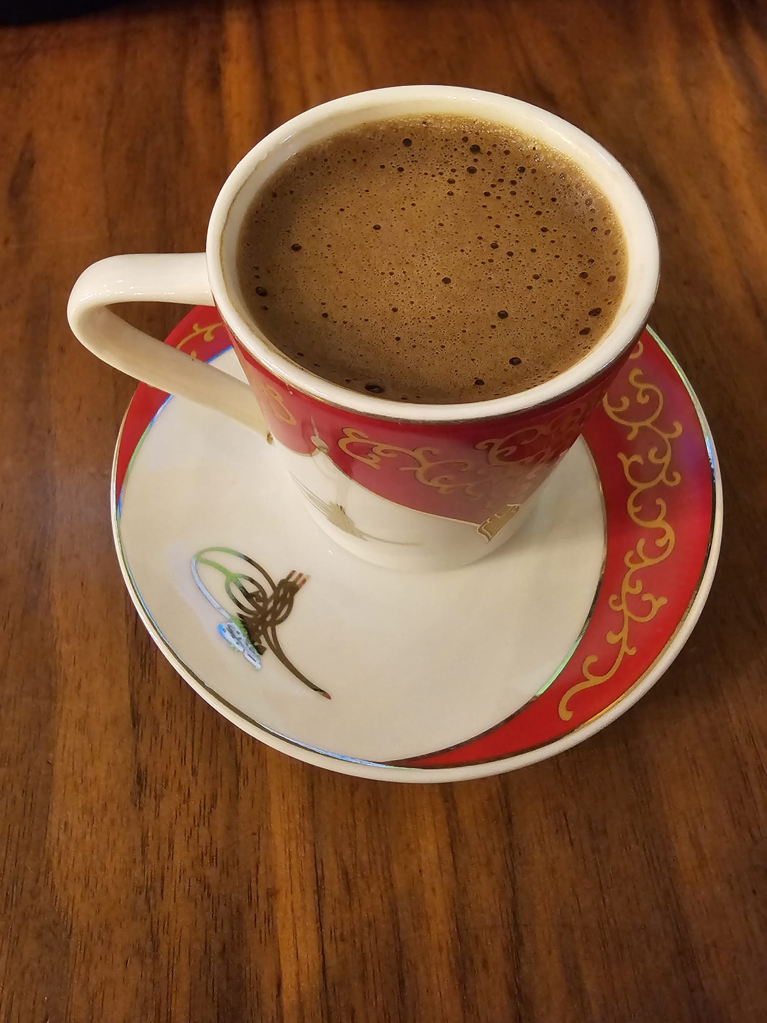 A traditional cup of dark Turkish coffee with a rich foam, served in a decorative red and white porcelain cup and saucer.