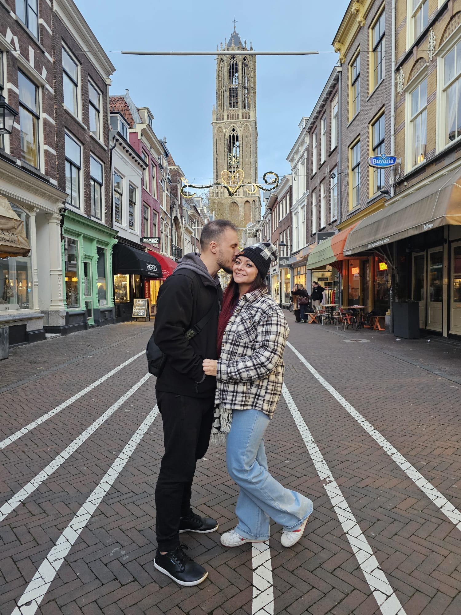 Couple sharing a kiss on a charming pedestrian shopping street in Utrecht with the Dom Tower visible in the background