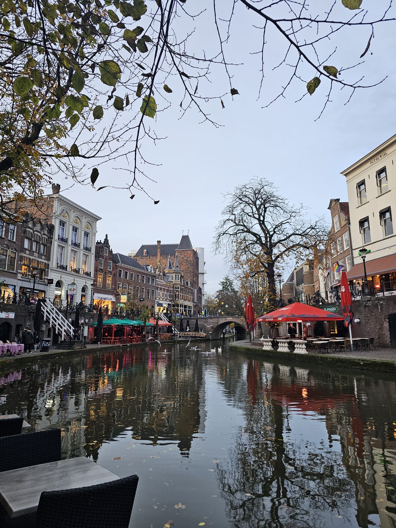 Bustling canal-side street with outdoor cafe seating, red umbrellas, and historic buildings lining the waterway in Utrecht, Netherlands