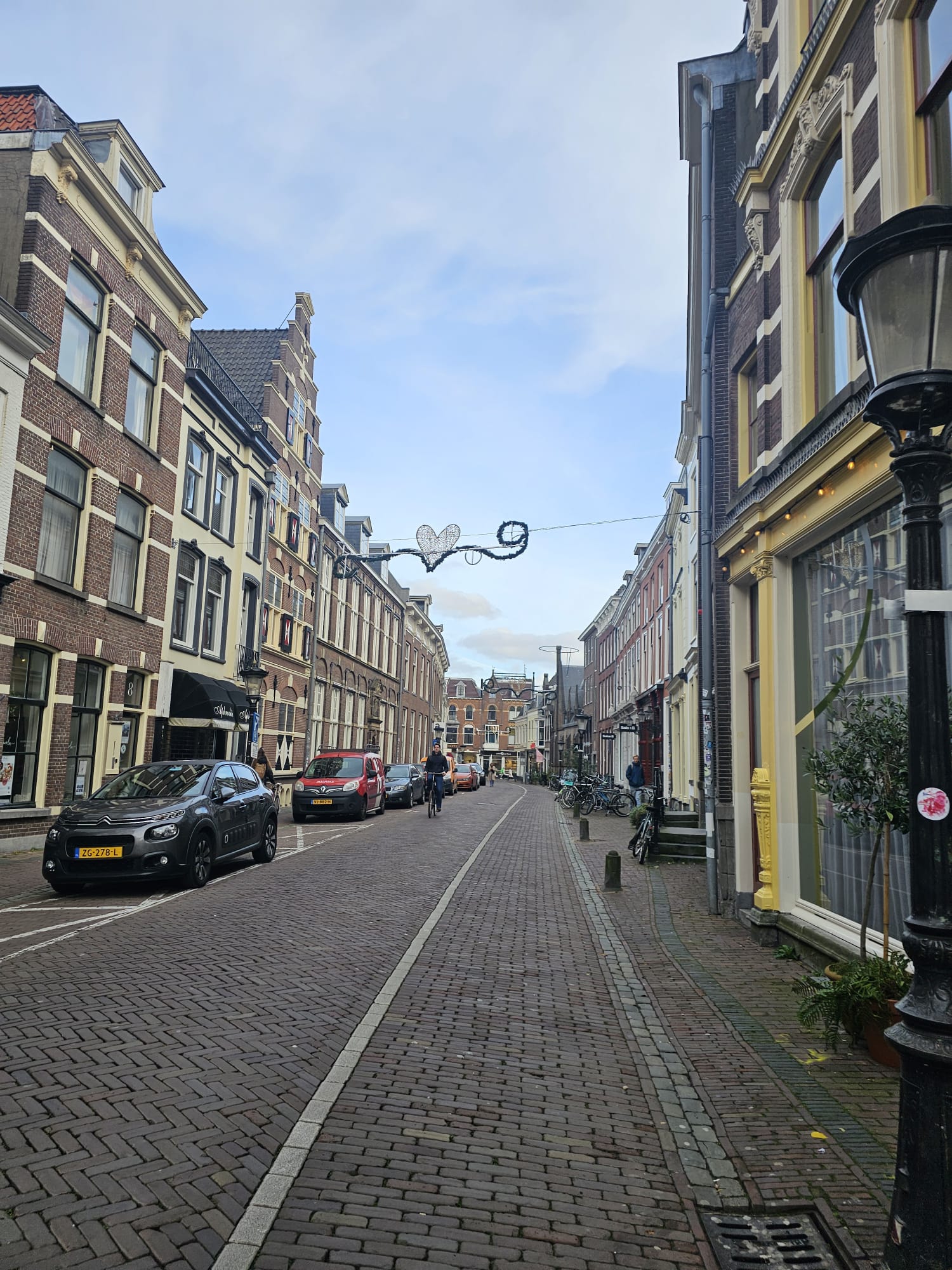 Narrow cobblestone street lined with traditional Dutch brick buildings and a decorative heart-shaped wire hanging overhead in Utrecht, Netherlands