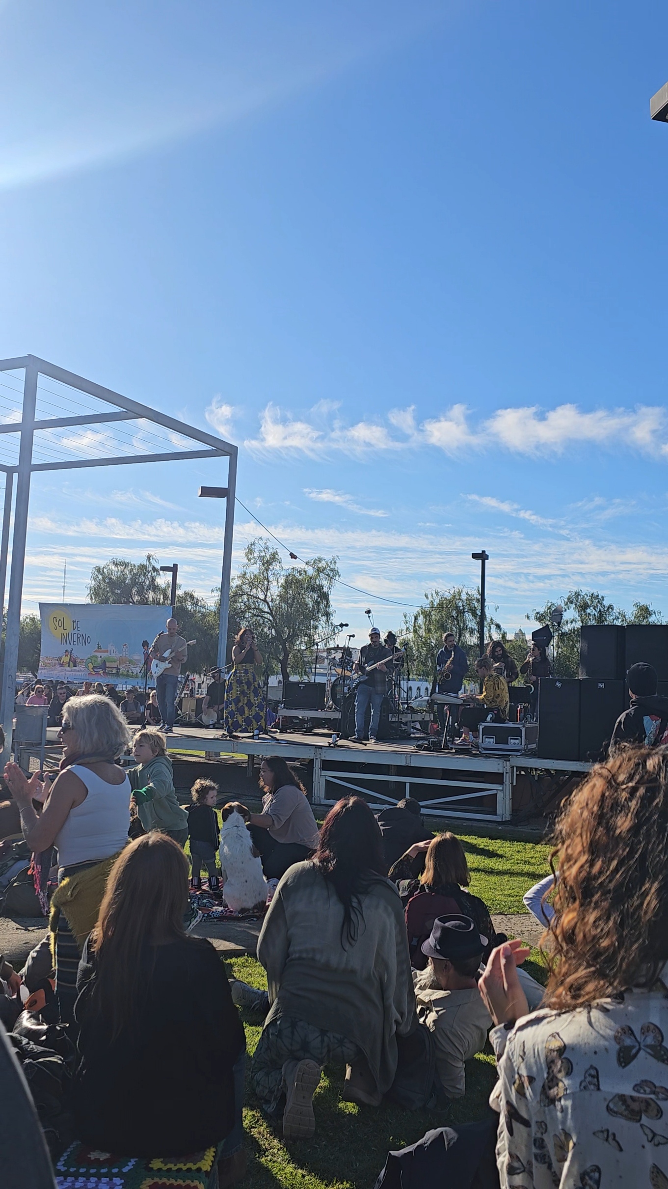 Crowd sitting on the grass watching a live outdoor concert performance on a sunny day at Sol de Inverno Festival in Portugal