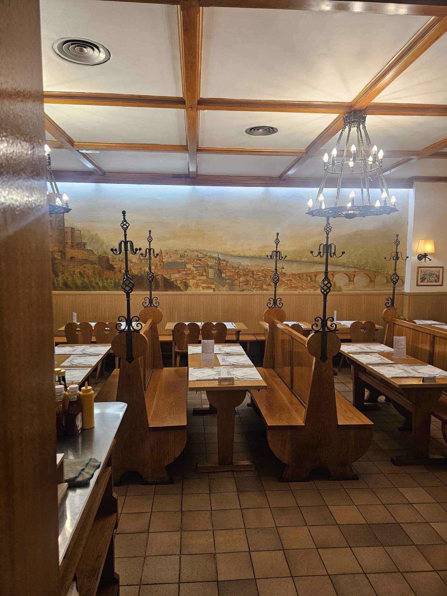 Traditional German brewery-style dining room with wooden benches, tables, chandeliers, and a scenic mural at Alt Heidelberg in Barcelona