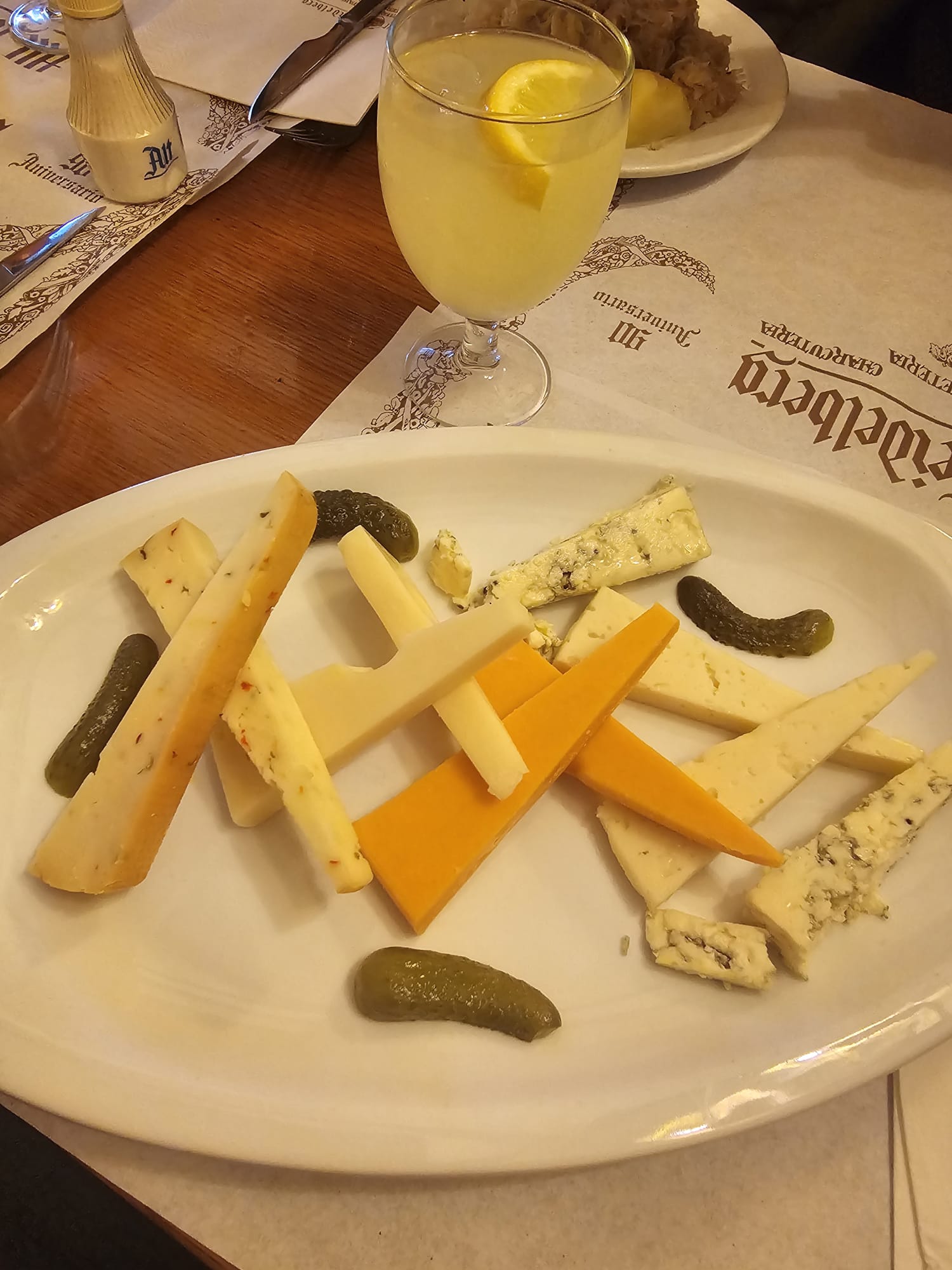 Assorted cheese plate with pickles and a glass of lemon water at Alt Heidelberg restaurant in Barcelona