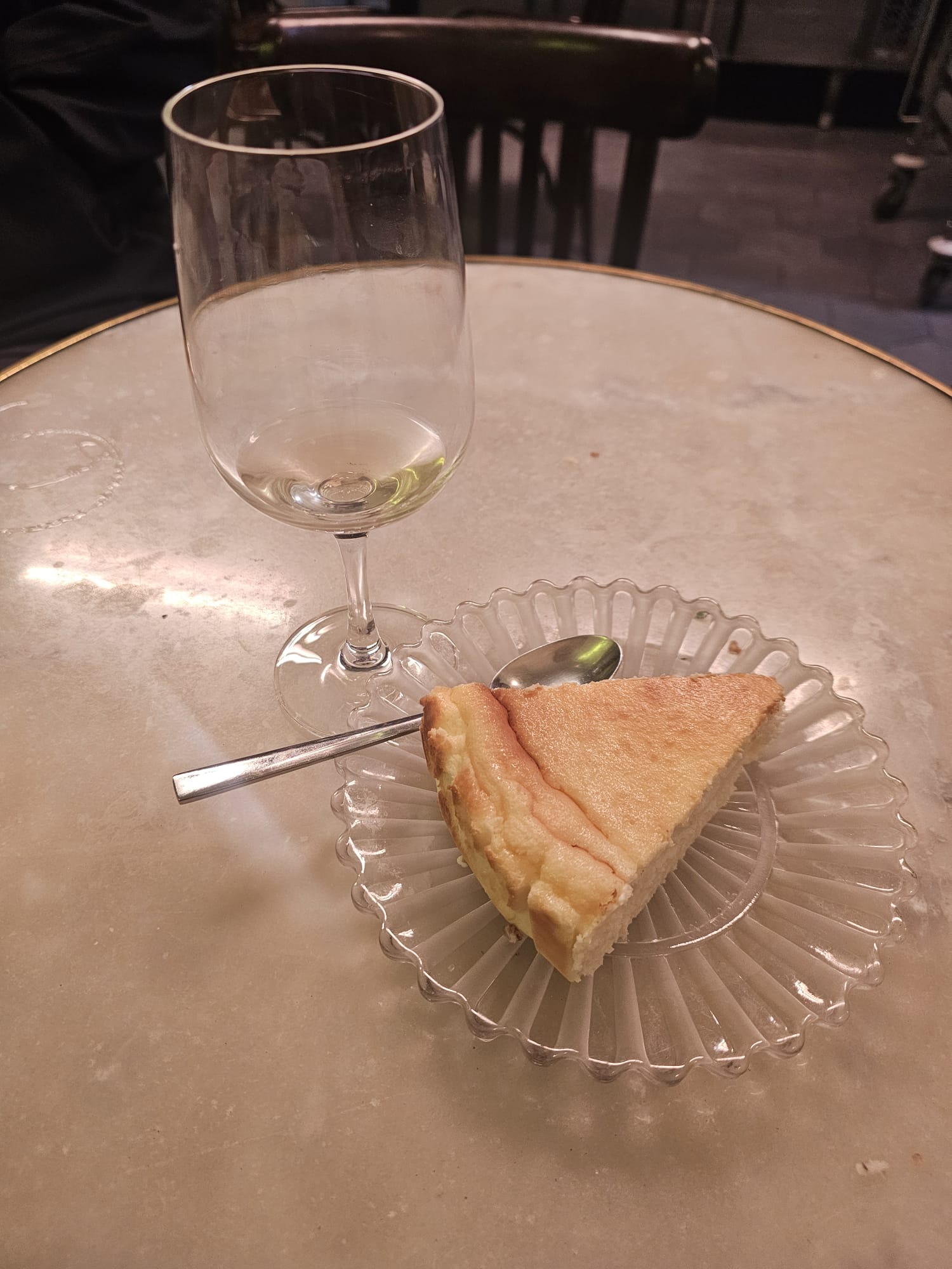 Slice of gluten-free cheesecake on a scalloped glass plate with a glass of white wine at The Fish and Chips Shop Gluten Free