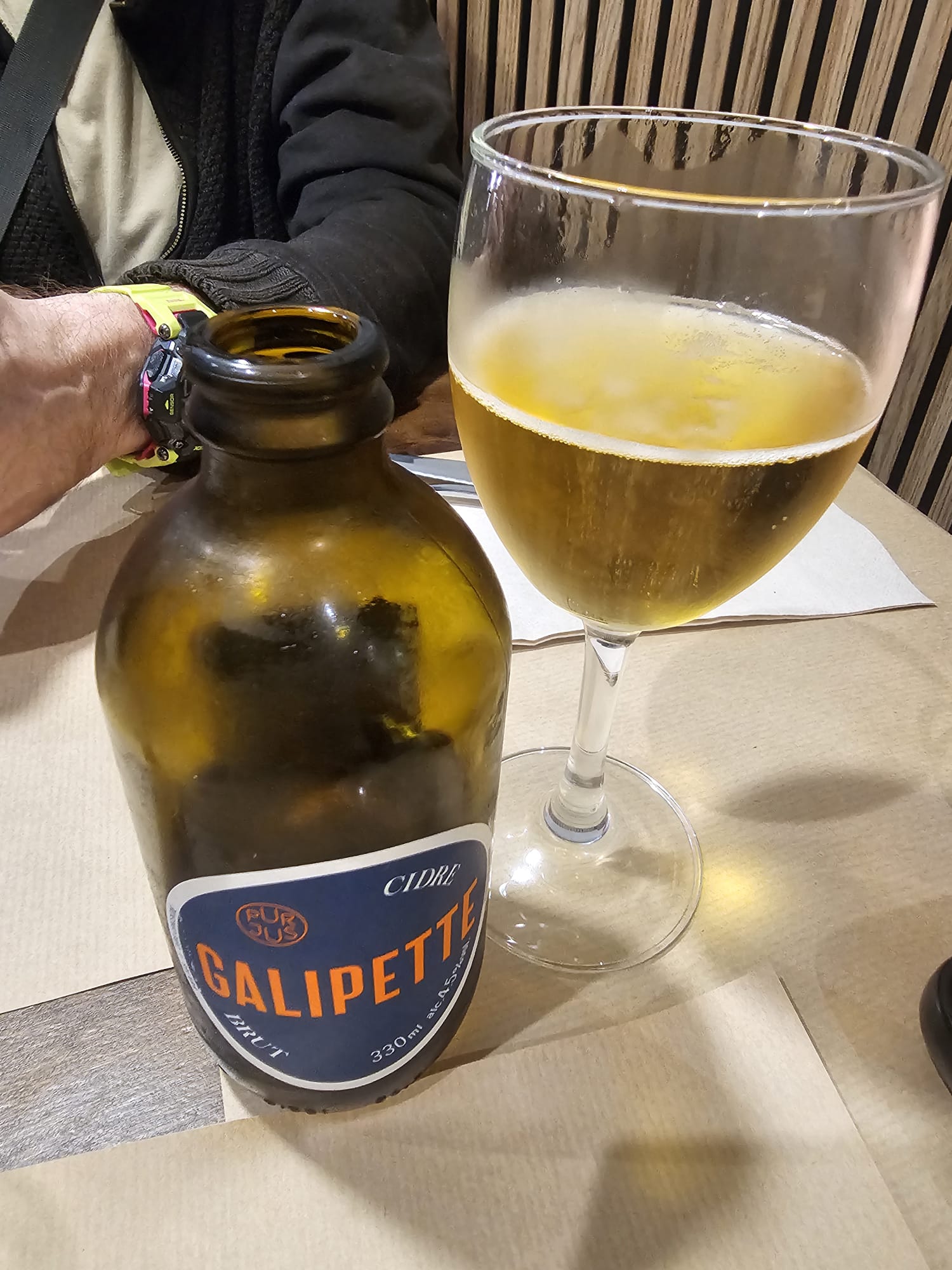 Bottle of Galipette French cider next to a glass of white wine on a restaurant table at Messie Pizza