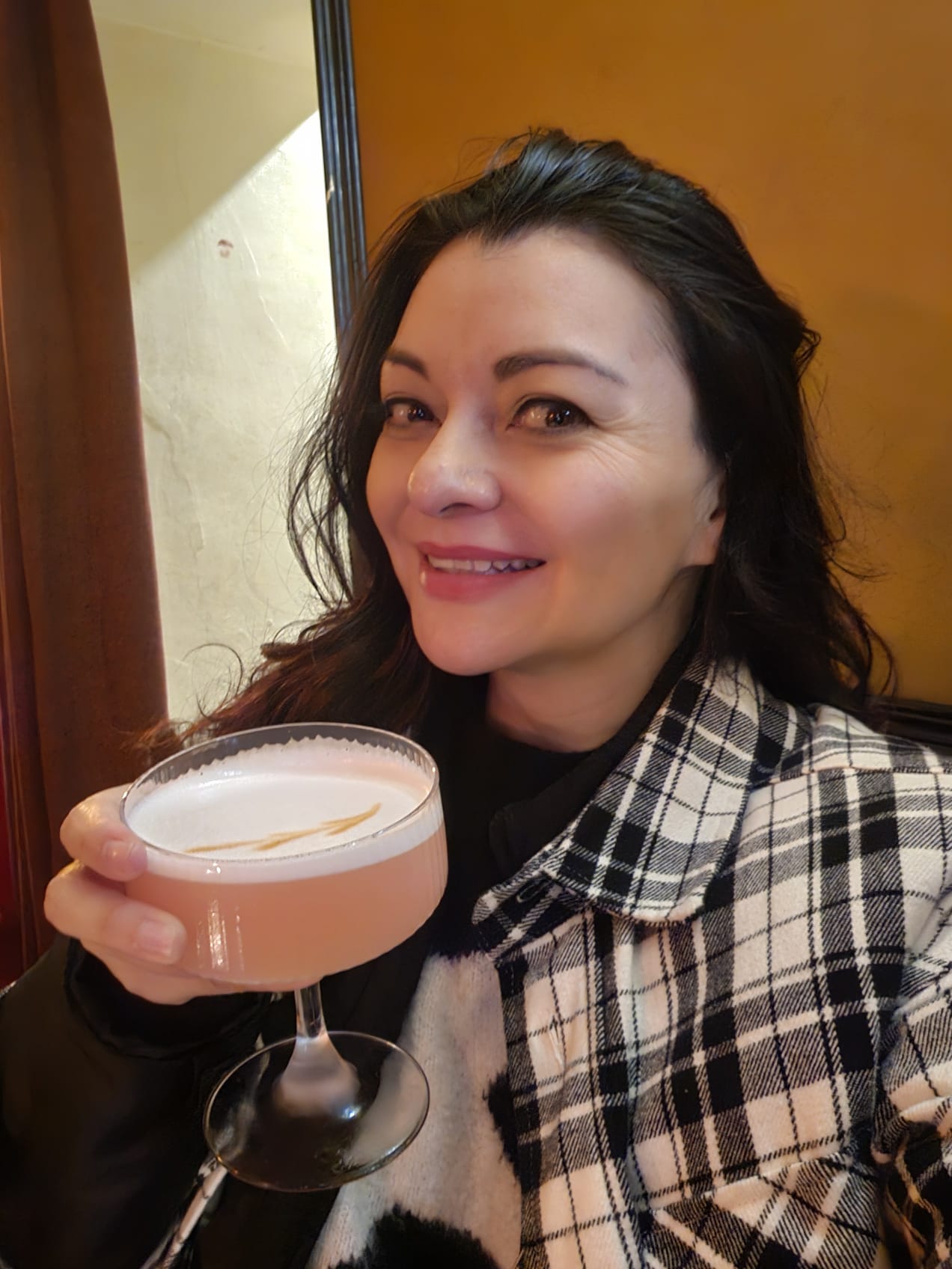 Woman smiling and holding a pink cocktail in a coupe glass at Cafe Bar l'ascensor in Barcelona