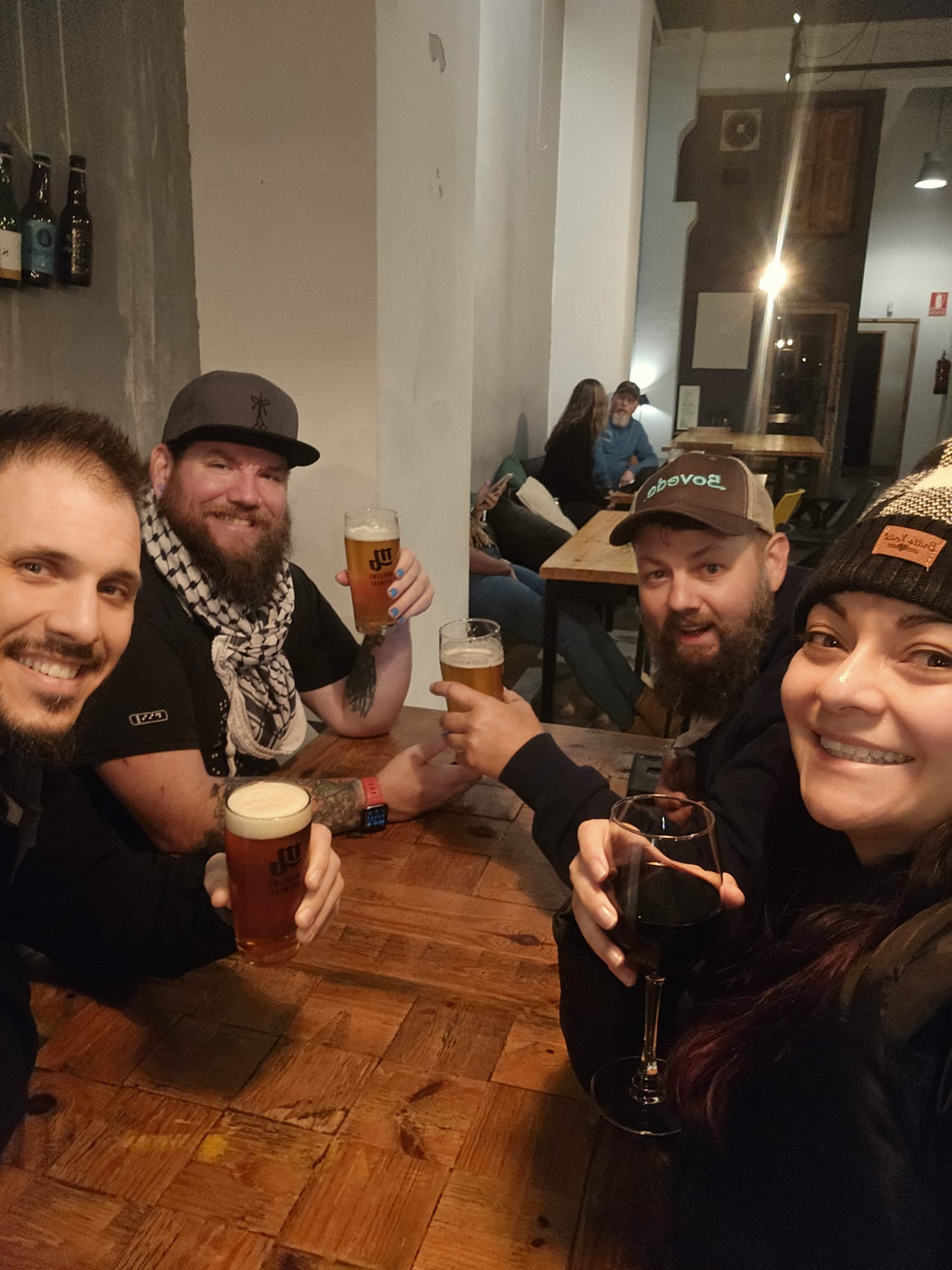 A group of 4 people. They are sitting at a table with drinks in hand and smiling at the camera