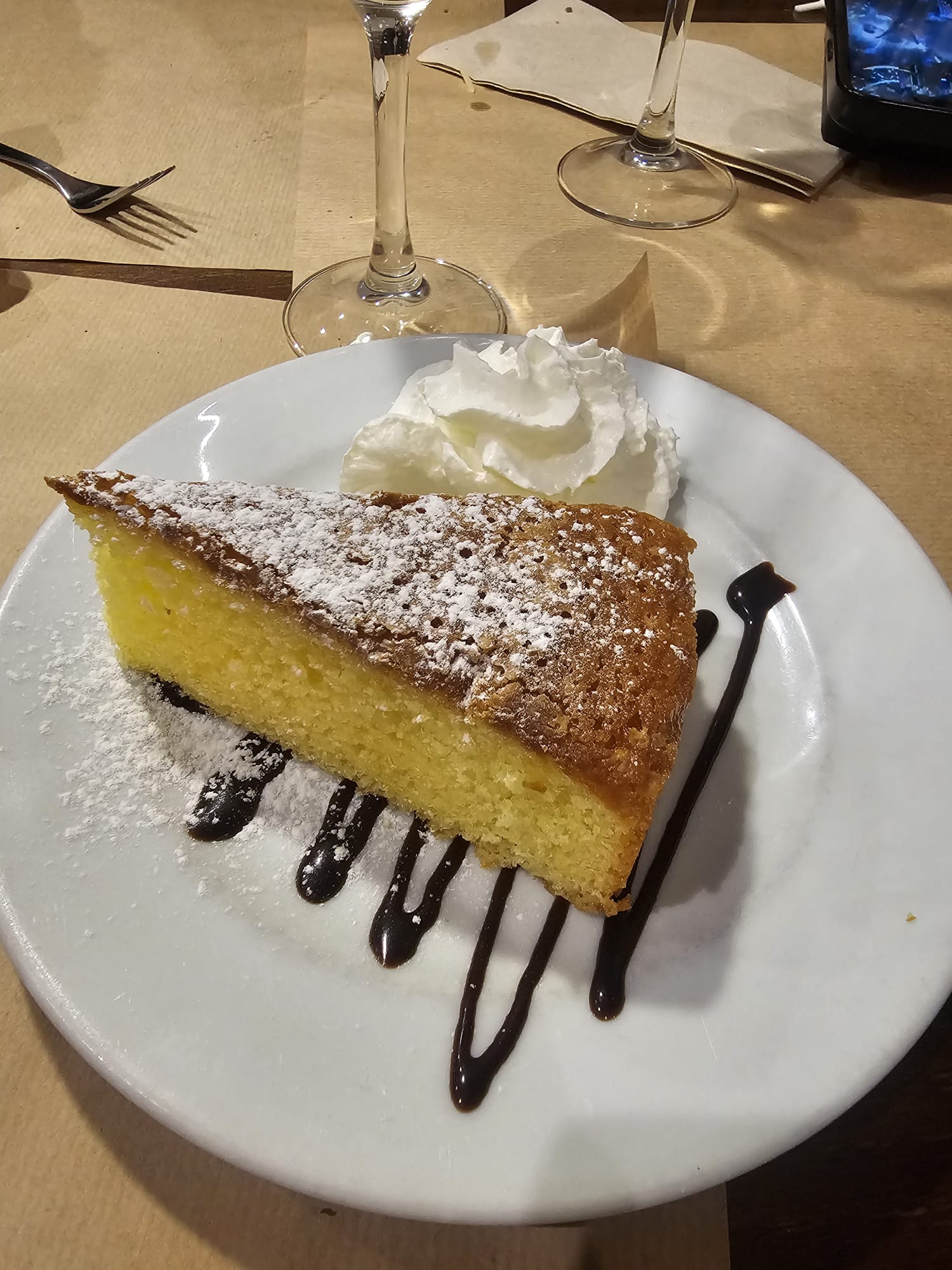Slice of gluten-free almond cake dusted with powdered sugar and served with whipped cream and chocolate sauce at Messie Pizza