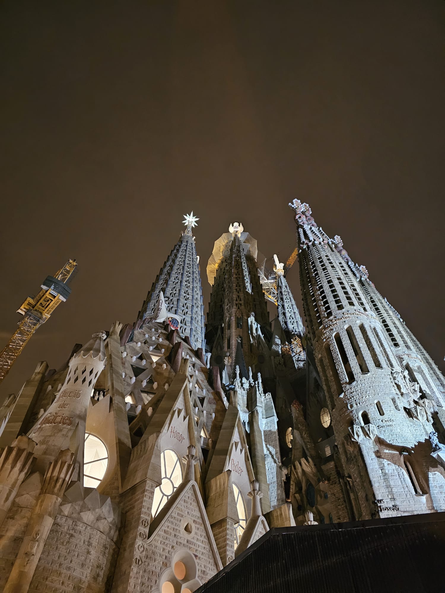 A low-angle, nighttime photo of the spires of the Sagrada Familia, illuminated against the dark sky. Text overlay reads: "La Sagrada Famila at night, isnt it magical?!