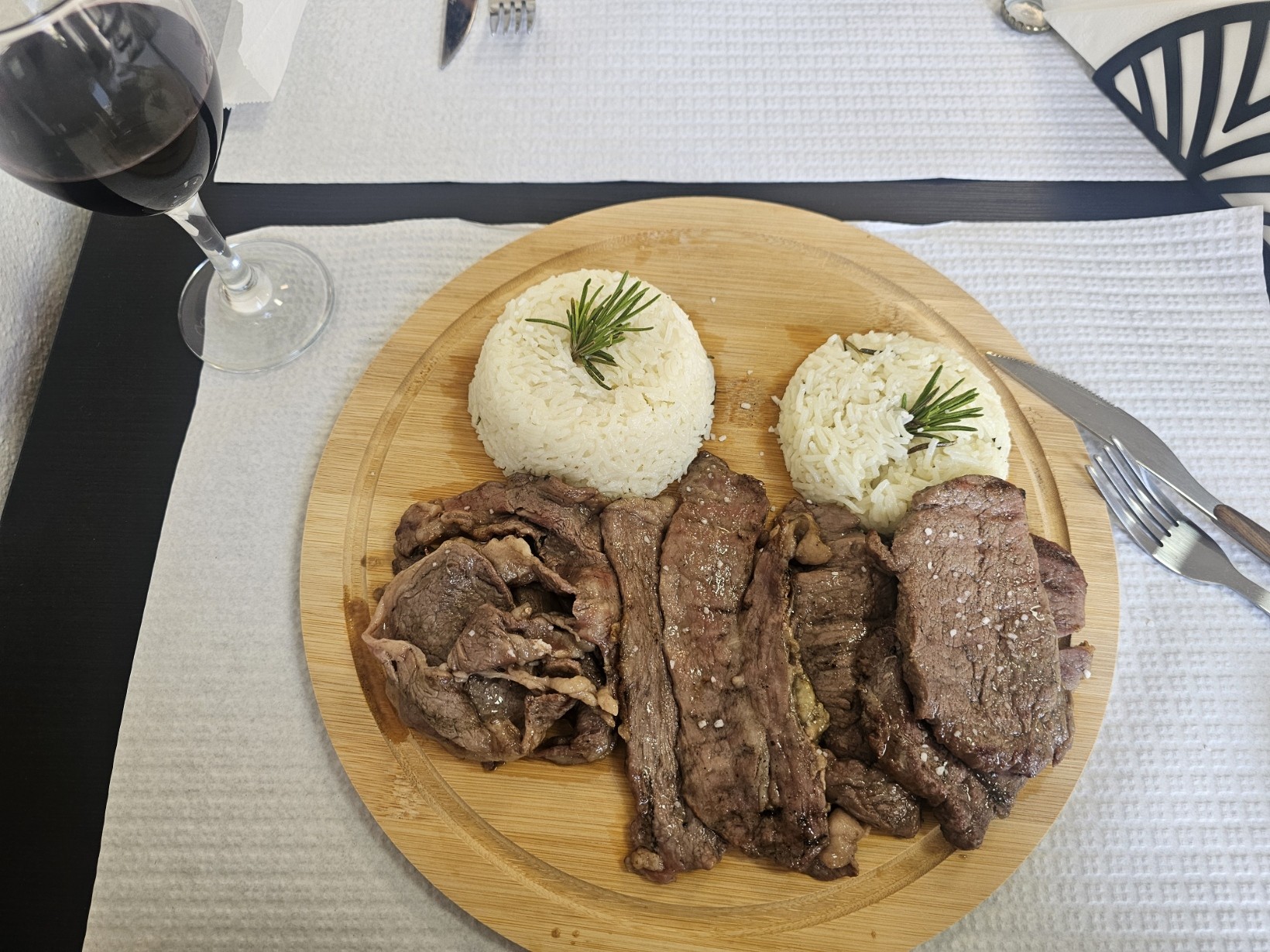 Mixed grill plate with three types of grilled meat and two mounds of white rice garnished with rosemary, served on a wooden board at Let's Meat restaurant in Beja, Portugal, with a glass of red wine in the background