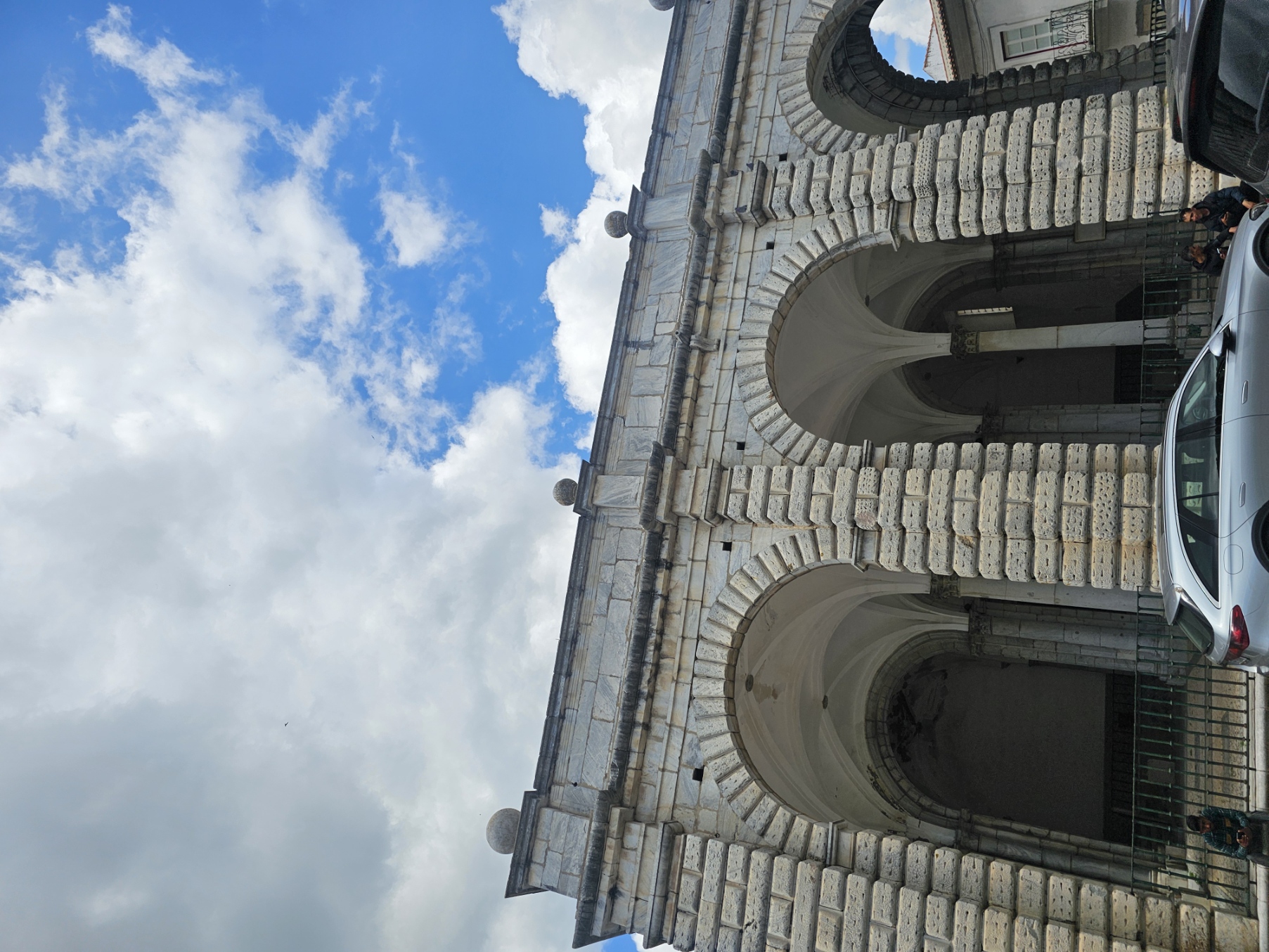 Looking up at the grand arched facade of Praça da Republica in Beja, Portugal, with white stone archways against a blue sky