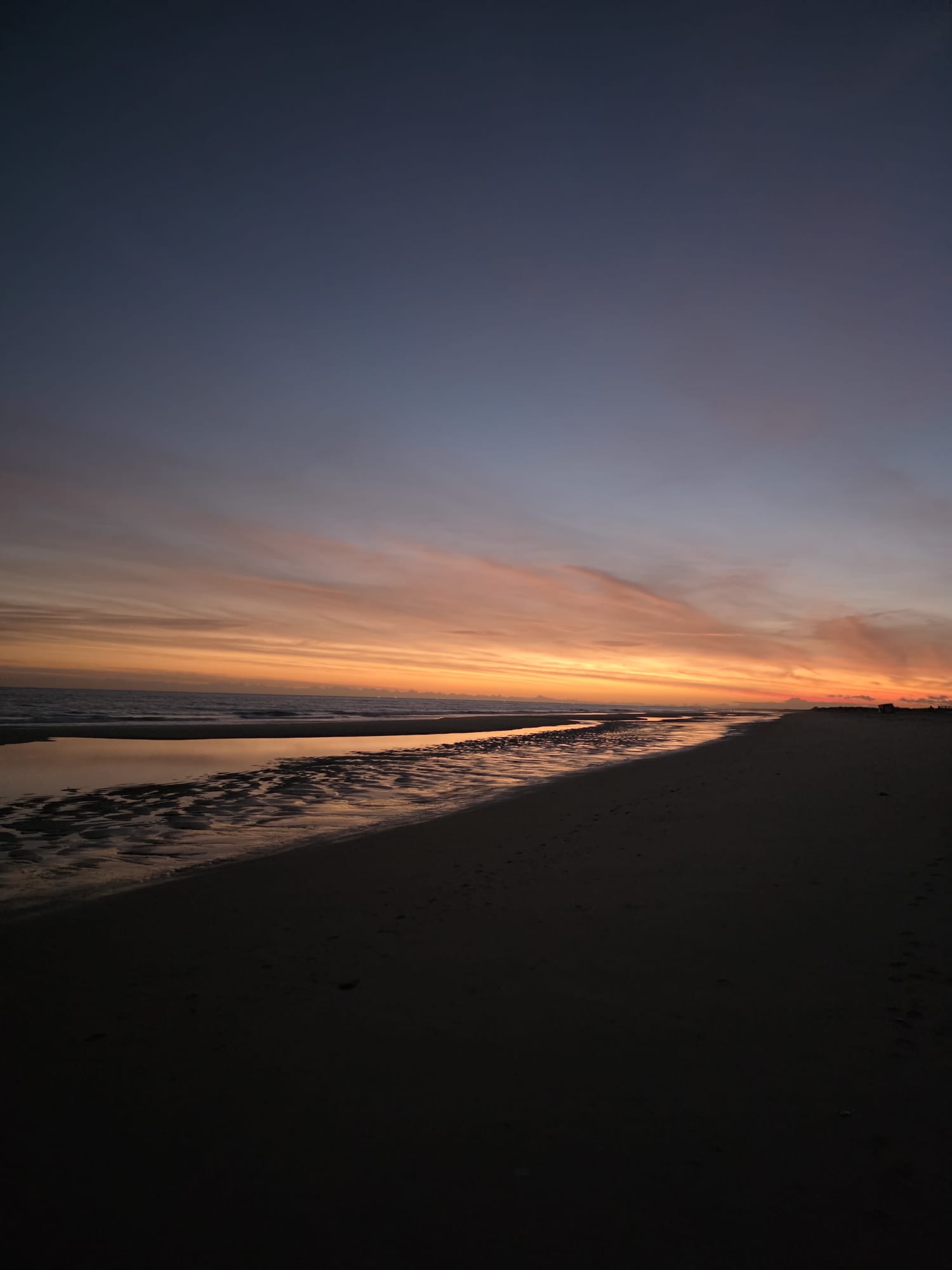 Dramatic sunset over Manta Rota Beach in the Eastern Algarve Portugal with vivid orange and pink streaks reflecting off the wet sand
