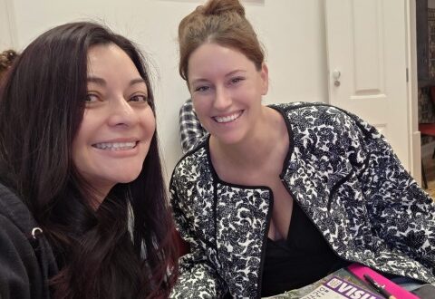 Two women smiling at a table with a European Portuguese language textbook during a language class in Portugal