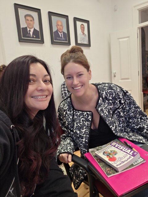 two women taking a selfie with a European Portuguese language book